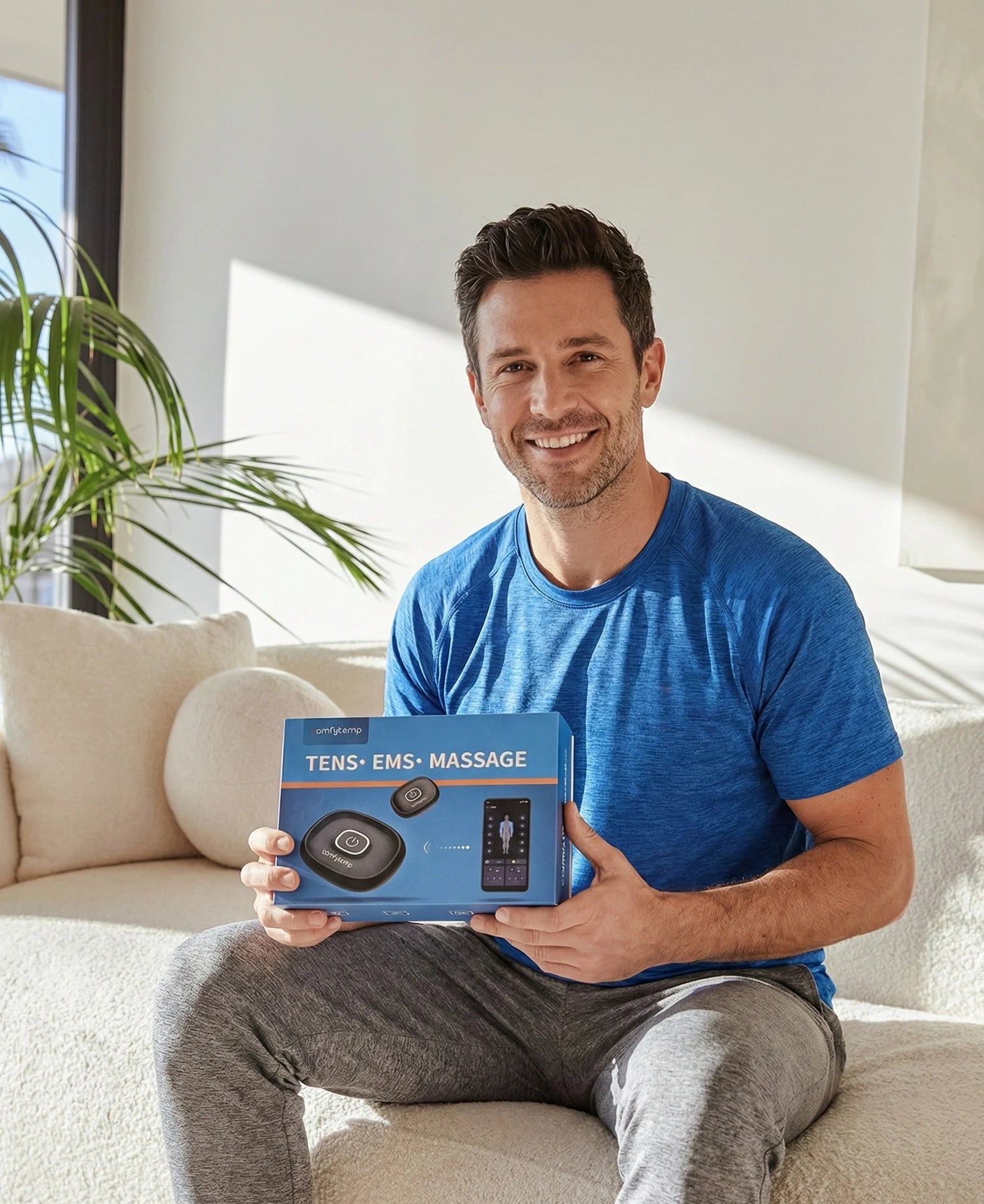 Man holding a TENS EMS massage device box in a living room.